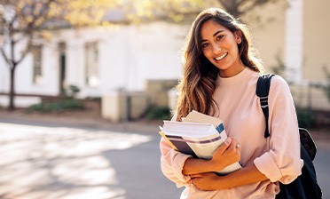 Smiling student holding textbooks on campus