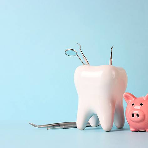 A large model tooth with dental tools next to a pink piggy bank
