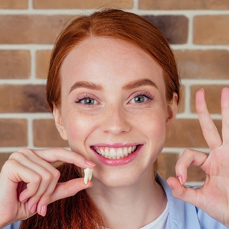 A smiling red-haired girl holding a wisdom tooth extracted from her mouth